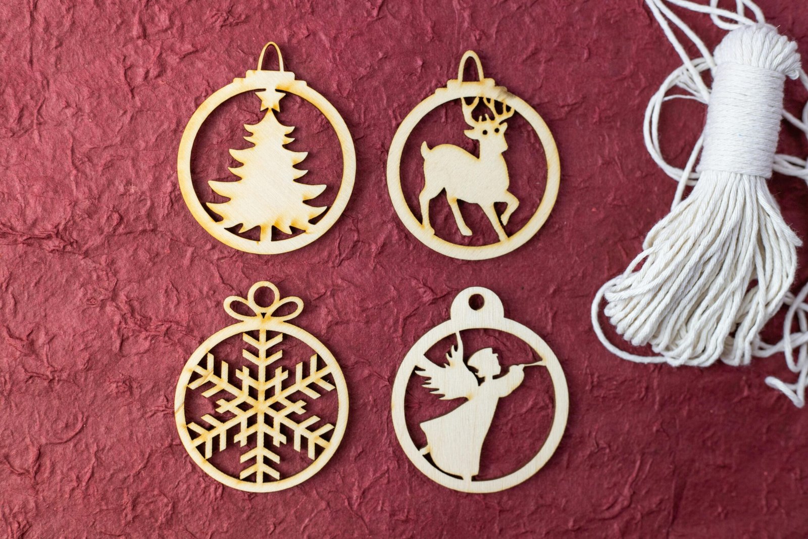 About Flat lay of wooden Christmas ornaments featuring tree, reindeer, angel, and snowflake on a textured red background.